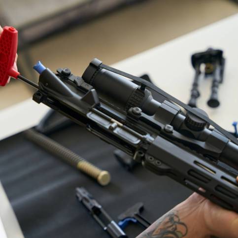 Man cleans a disassembled firearm with a special tool on a napkin, parts of the machine gun are laid out